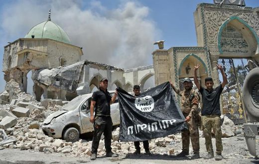 In this file photo taken on June 30, 2017 a member of Iraq's counter-terrorism squad flashes a victory sign as others hold upside-down an Islamic State group flag outside Al-Nuri Mosque in Mosul's Old City after IS was ousted from the area