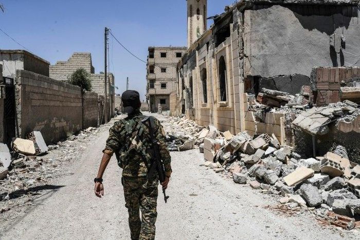 A member of the Syrian Democratic Forces (SDF), an alliance of Kurdish and Arab fighters, walks on a damaged street in western Raqa