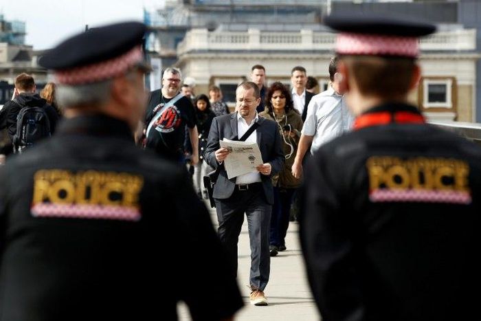 Police officers stand on duty as commuters walk across London Bridge in London on June 5, 2017, after it was partially re-opened following the June 3 terror attack