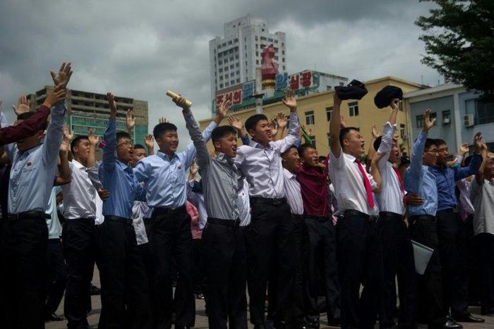 People gesture as coverage of an ICBM missile test is displayed on a screen in a public square in Pyongyang