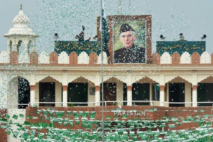 The portrait of Muhammad Ali Jinnah is seen at the India-Pakistan Wagah border post as a Pakistani Ranger (top) unfurls the national flag on Independence Day