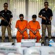 Indonesian narcotics police guard two suspects and the seized drugs during the press conference