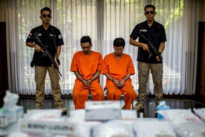 Indonesian narcotics police guard two suspects and the seized drugs during the press conference