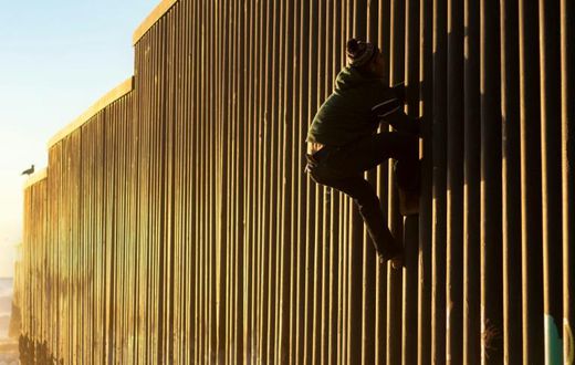A Honduran migrant climbs the US-Mexico border fence on December 8, 2018