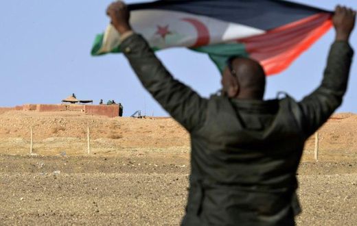 A Saharawi man holds up a Polisario Front flag in the Al-Mahbes area near Moroccan soldiers guarding the wall separating the Polisario controlled Western Sahara from Morocco on February 3, 2017