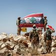 Hezbollah fighters giving a guided tour near the Lebanese-Syrian border on July 26, 2017 raise a Lebanese flag showing pictures of soldiers killed fighting jihadists