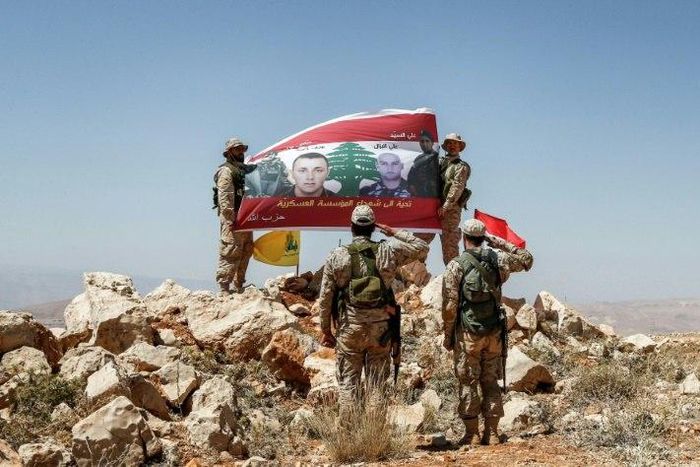 Hezbollah fighters giving a guided tour near the Lebanese-Syrian border on July 26, 2017 raise a Lebanese flag showing pictures of soldiers killed fighting jihadists