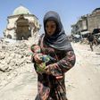 An Iraqi woman carrying a child walks by the destroyed Al-Nuri Mosque as she flees the Old City of Mosul on July 5, 2017