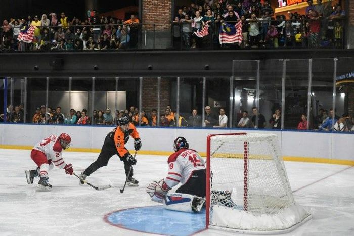 Malaysia's Jun Ming Low (C) dribbles the puck past Indonesia's goalkeeper Sangga Munggaran Putra (R) during their ice hockey match at the 29th Southeast Asian Games (SEA Games) in Kuala Lumpur on August 20, 2017