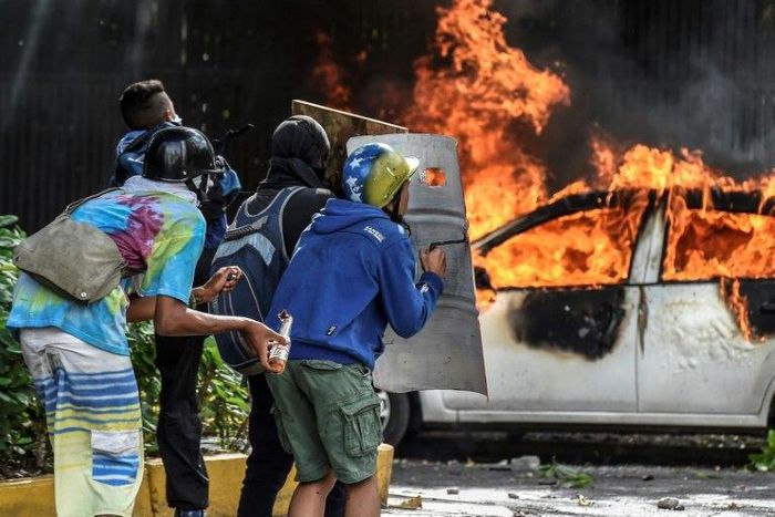 Anti-government demonstrators take cover behind shields near a burning car during clashes near Altamira Square in Caracas, on June 14, 2017
