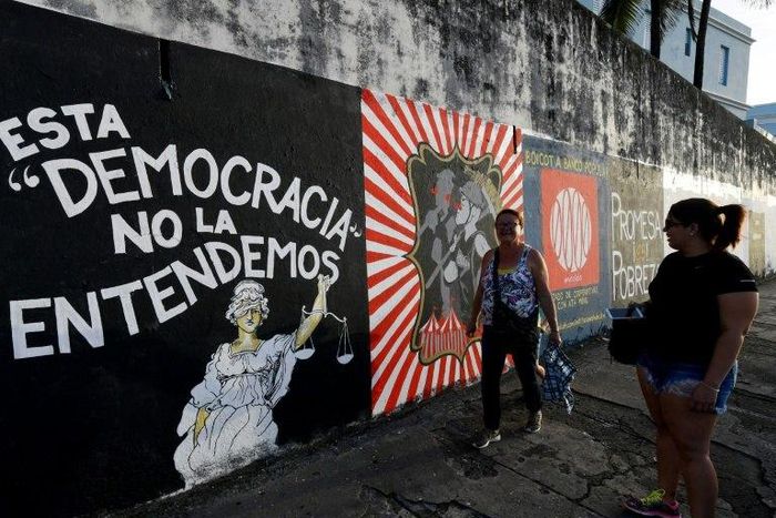 People walk past murals protesting the state of the economy in San Juan, Puerto Rico, as the former Spanish colony of 3.5 million, now a US territory, struggles under a mountain of debt