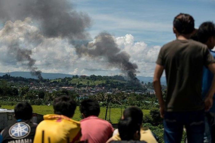 People watch as smoke rises from houses after Philippine air force planes bombed Islamist militant positions in the city of Marawi on the southern island of Mindanao