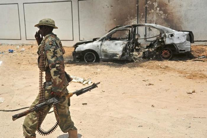 A Somali soldier patrols next to the burnt-out wreckage of a car that was used by suspected Al-Shabab fighters, which increasingly have been targeted by the US military
