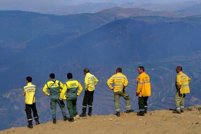 Members of a fire brigade stand on a cliff after extinguishing a wildfire near the village of Santa Eugenia, northern Portugal's Alijo municipality, on July 18, 2017