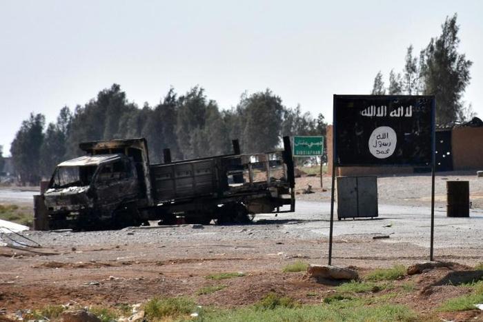 A burnt-out vehicle is seen next to the Islamic State group's flag on the outskirts of the Syrian city of Raqa on June 11, 2017