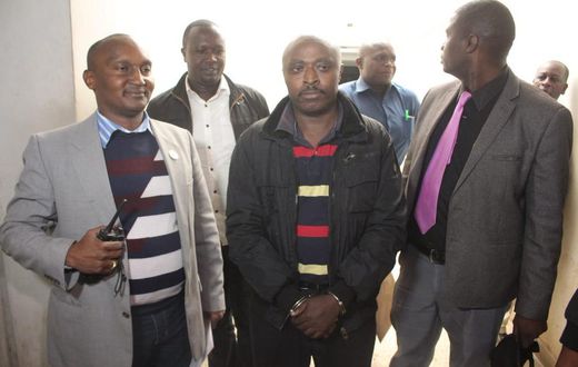 Mugo wa Wairimu escorted by police officers during his court appearance