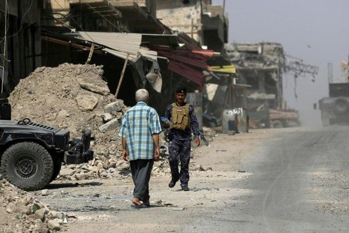 A man walks past a member of the Iraqi forces in west Mosul a few days after the city's recapture from Islamic State fighters