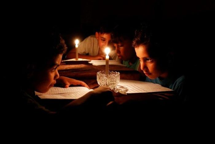 A picture taken on June 13, 2017 shows Palestinian children at home reading books by candle light due to electricity shortages in Gaza City