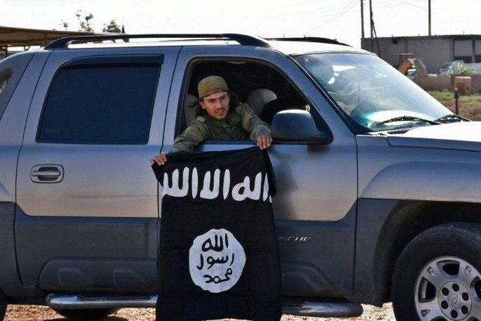 A member of the Syrian pro-government forces holds an Islamic State (IS) group flag after they entered the village of Dibsiafnan on the western outskirts of the Islamist's Syrian bastion of Raqa on June 11, 2017