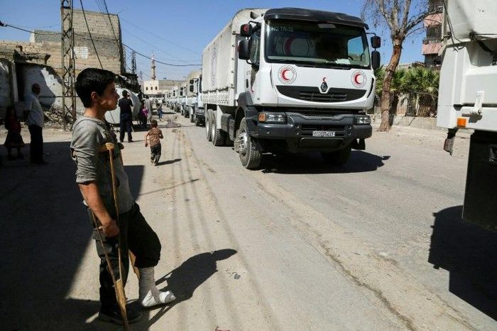 A young injured Syrian looks at United Nations and Syrian Arab Red Crescent convoy trucks arriving in the rebel-held town of Nashabiyah in eastern Ghouta on July 30, 2017 to deliver aid packages for the first time in five years