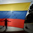 A protester's shadow is cast on a Venezuelan national flag in Caracas, the capital city of a country that has hit its 100th day of anti-government protests