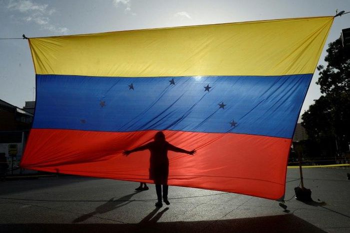 A protester's shadow is cast on a Venezuelan national flag in Caracas, the capital city of a country that has hit its 100th day of anti-government protests