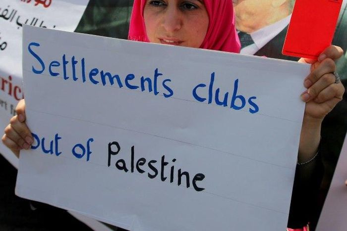 A Palestinian woman holds a red card and a banner opposing the participation in the Israeli league clubs located in Jewish settlements in the occupied West Bank, during a protest in Ramallah May 19, 2015