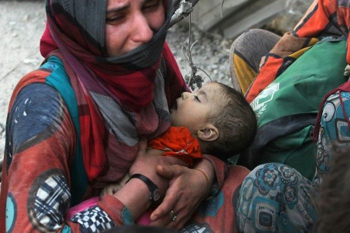 An Iraqi woman carries a child as she flees the Old City of Mosul on July 5, 2017