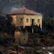 A man stands in the stairway of a house with smoke billowing from the roof in an area devastated by a wildfire in Canical, near Alvares, on May 18, 2017
