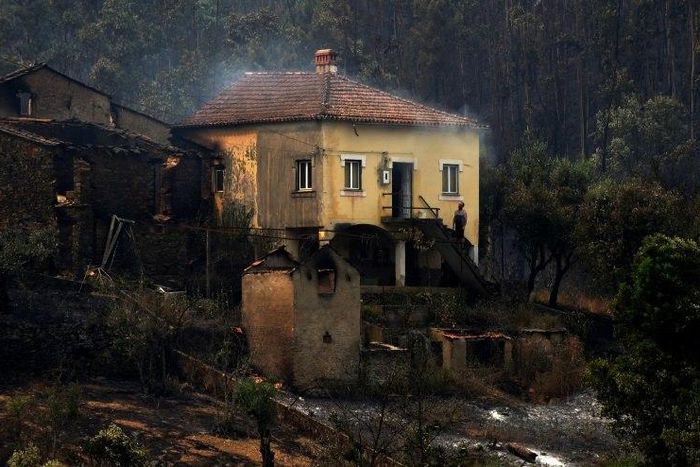 A man stands in the stairway of a house with smoke billowing from the roof in an area devastated by a wildfire in Canical, near Alvares, on May 18, 2017