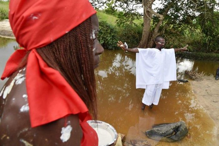 A member of a traditional group stands in the Bodo River with an egg in either hand during the inauguration ceremony of a memorial stone on a site of the former slave route in the Ivorian hamlet of Kanga Gnianze, northwest of Abidjan