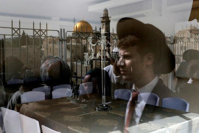 A picture taken through the window of a restaurant shows a reflection of Jews taking part in the Passover priestly blessing at Jerusalem's Western Wall on April 13, 2017, with the Dome of the Rock seen in the background