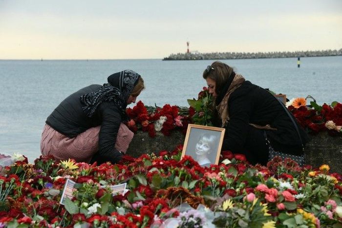 People lay flowers next to a portrait at a makeshift memorial in Sochi, on December 27, 2016 after a military plane carrying 92 people, including dozens of members of the Red Army Choir, crashed in the Black Sea