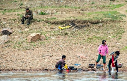 A North Korean soldier reads a book near women washing clothes in the Yalu border river on April 16, 2017