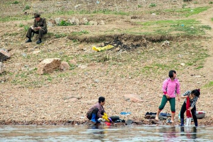 A North Korean soldier reads a book near women washing clothes in the Yalu border river on April 16, 2017