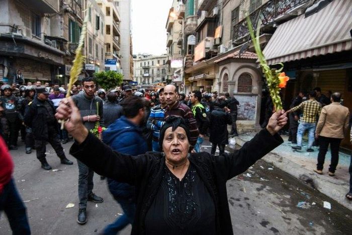 An Egyptian woman raises braided palm leaves, originally intended for Palm Sunday celebrations, during a gathering outside the Coptic Orthodox Patriarchate in Alexandria after a bomb blast struck outside while worshippers attended Palm Sunday mass on A...