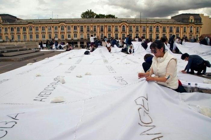 People sew white sheets with names of victims of the Colombian conflict painted in ash on them, in Bolivar square, Bogota