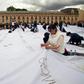 People sew white sheets with names of victims of the Colombian conflict painted in ash on them, in Bolivar square, Bogota