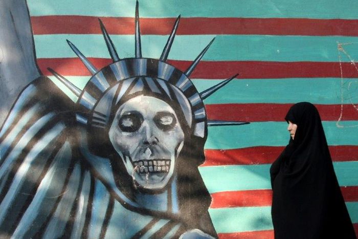 An Iranian woman walks past a mural on the wall of the former US embassy in Tehran