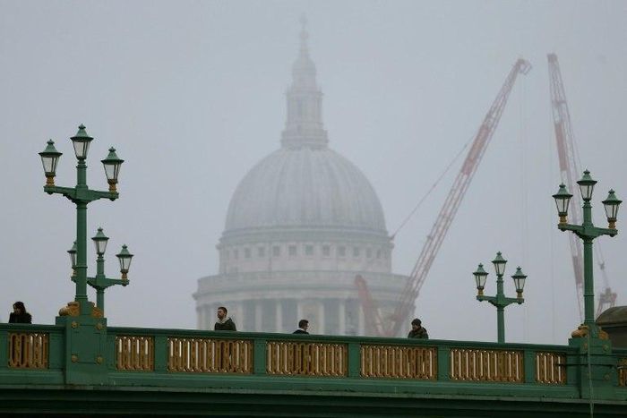 Pedestrians walk through the fog as they cross Southwark Bridge in London as St Paul's Cathedral looms in the background on January 23, 2017