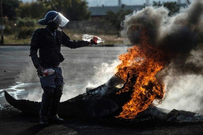 A policeman tries to extinguish a fire after demonstrators burnt tyres to barricade a road during violent protests in Ennerdale