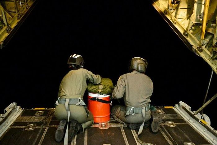 US Coast Guard officers sit on the ramp of an HC-130 Hercules and prepare to deploy a long range drop kit to a disabled vessel approximately 80 miles off Tonga