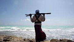 An armed Somali pirate walks along the coastline near Hobyo in 2010