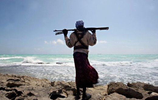 An armed Somali pirate walks along the coastline near Hobyo in 2010