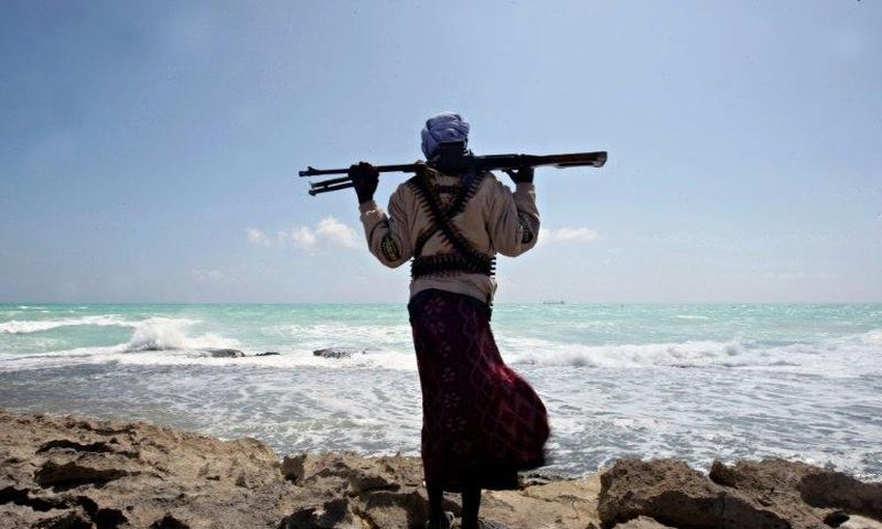 An armed Somali pirate walks along the coastline near Hobyo in 2010