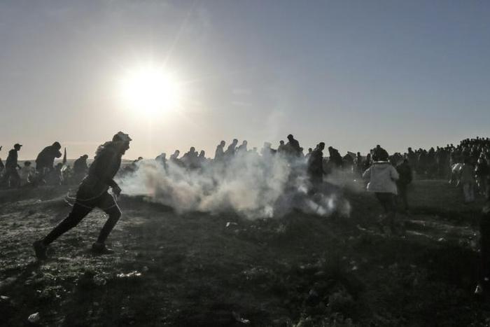 Palestinian protesters run through tear gas during clashes with Israeli forces following a demonstration at the border of the Gaza Strip on January 11, 2019