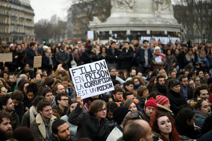 A man holds a placard reading "Fillon to prison, corruption is a poison" a he sits in place de la Republique in Paris, on February 19, 2017 during a rally to protest against the corruption of the elected politicians