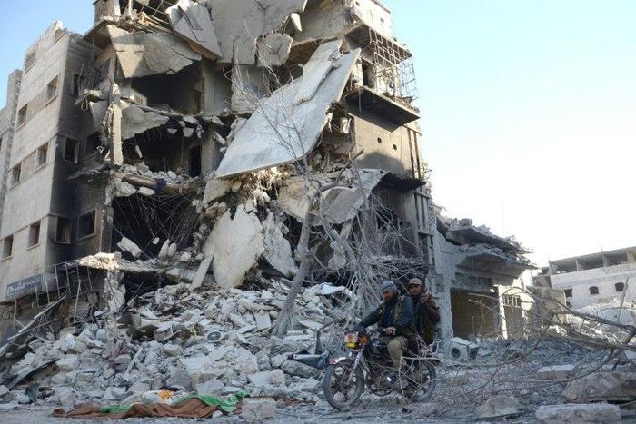 Rebels ride a motorcycle past a destroyed building in the northwestern Syrian border town of al-Bab on February 25, 2017