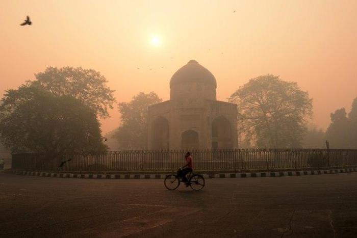 A cyclist rides along a street as smog envelops a monument in New Delhi on October 31, 2016, a day after the Diwali festival