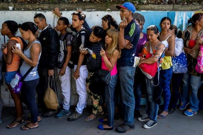 People queue to buy basic food and household items outside a supermarket in Caracas, on September 28, 2016